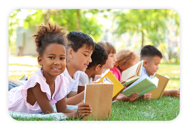 a group of children reading books on a grassy lawn