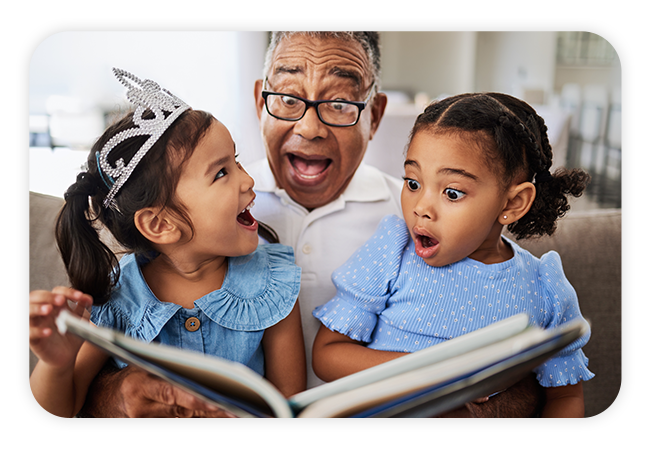 Man reading a book to two surprised young girls in blue dresses.