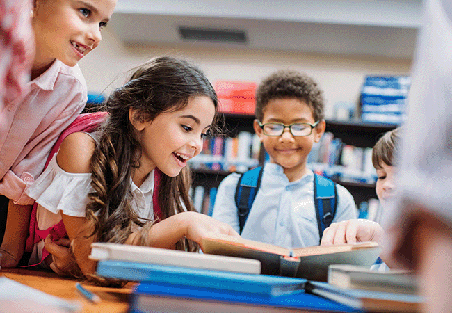 children excitedly leaning over a stack of books on a table